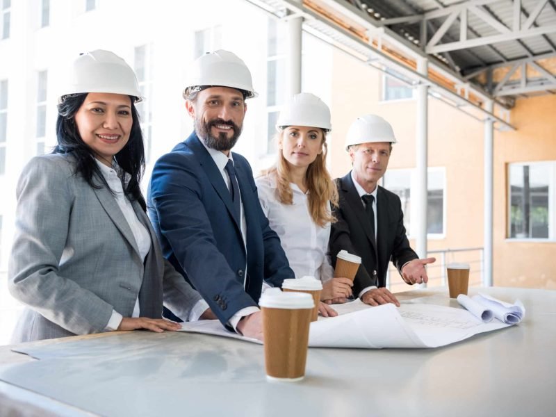 group of multiethnic architects in suits looking at camera while working with blueprints