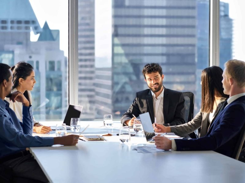 Happy international multiethnic professional business team, diverse executive colleagues people discussing financial project working together in office at group meeting table in corporate board room.