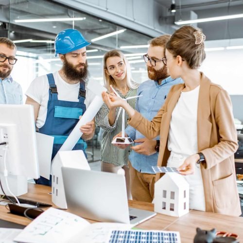 Group of engineers and workman working on a project of alternative energy at the office with computer, wind turbine and solar panels model